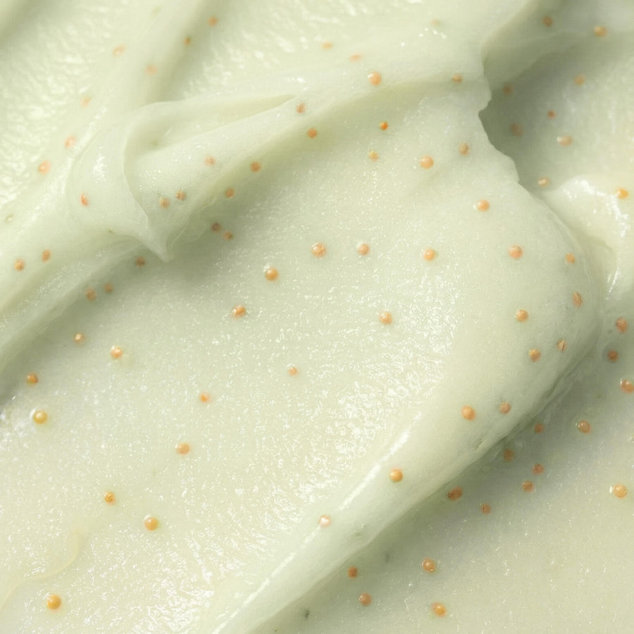 A close-up of a thick, creamy off-white cosmetic or skincare cream with tiny orange specks throughout, showing a smooth, swirled texture.