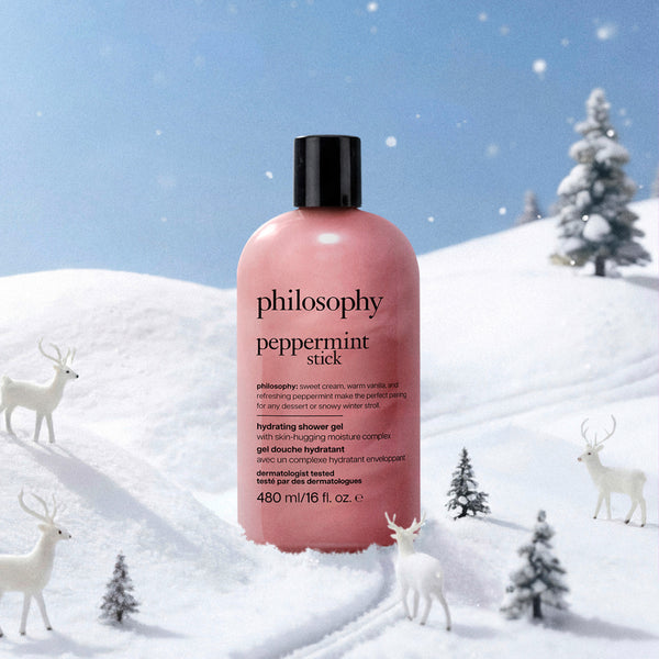 A pink bottle of Philosophy Peppermint Stick hydrating shower gel stands in a snowy winter scene with white deer and small pine trees under a blue sky.
