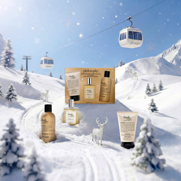 Fresh skincare gift set arranged in a snowy mountain landscape with ski lifts and snowmobile tracks. The set includes a gold-toned boxed collection, a bottle, a tube, and a small bottle with black caps, styled as if outdoors in winter snow.