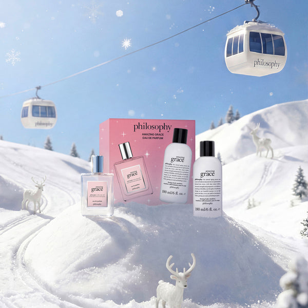 Philosophy Grace Smoothing Face Emulsion set displayed in a snowy mountain scene with cable cars and white deer figurines. The set includes a pink box, a pink bottle, a white bottle, and a white bottle with black caps.