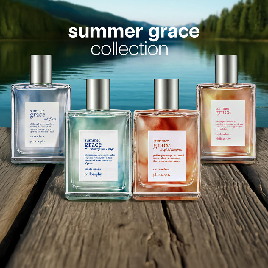 Four bottles of philosophy 'summer grace' collection on a wooden surface with a scenic background.