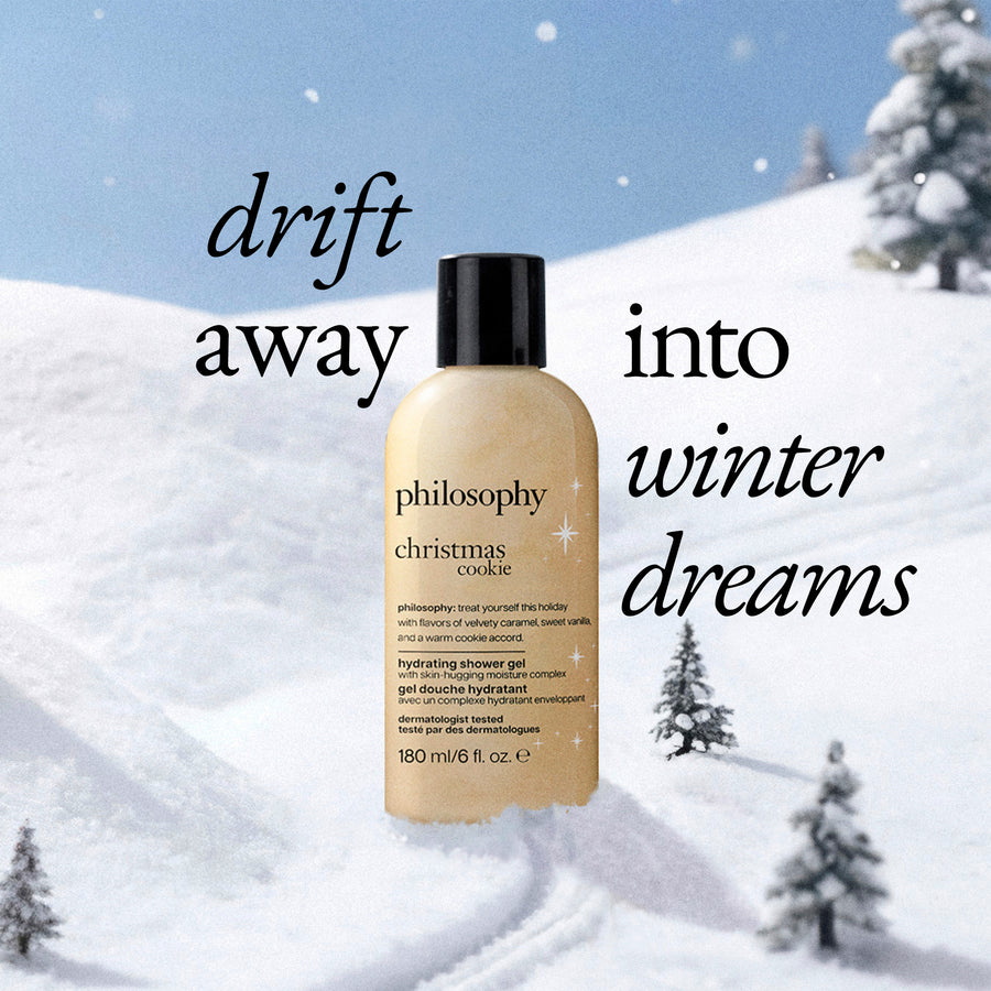 A bottle of Philosophy Christmas Cookie hydrating shower gel stands in a snowy winter landscape with the text 'drift away into winter dreams' on a blue sky background.