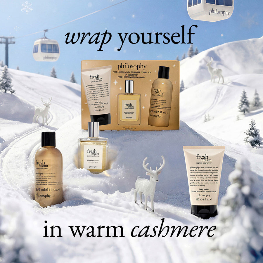 Philosophy body care set arranged in a snowy mountain scene with gondolas and deer. The set includes a boxed treatment, a bottle, a spray bottle, and a tube, with text reading 'wrap yourself in warm cashmere'.
